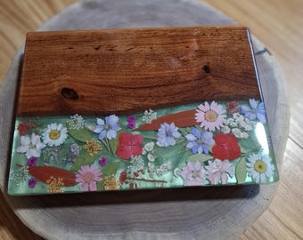 May include: A rectangular decorative tray featuring a dark brown wood section with visible grain and knots, joined to a clear resin section embedded with a variety of pressed colorful flowers, including pink, red, white, and blue blossoms and green leaves.