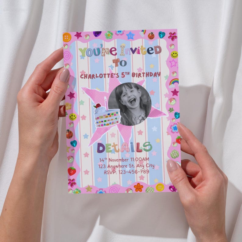 A colorful birthday invitation is held between two hands. The card has pastel stripes and a border filled with playful stickers like stars, hearts, smiley faces, rainbows, strawberries, and flowers. In the center, a round black‑and‑white photo of a smiling child sits beside a cute birthday cake illustration. The bright, crafty design creates a fun, whimsical celebration feel.