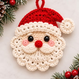 Könnte beinhalten: Ein gehäkelter Weihnachtsmann-Anhänger mit einer roten Mütze und weißem Bommel, einem cremefarbenen Bart und Schnurrbart, zwei schwarzen Kunststoffaugen, einer kleinen roten Nase und rosa Wangen. Oben befindet sich eine kleine Schlaufe.