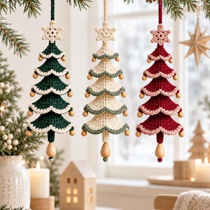 May include: Three hanging crochet Christmas tree ornaments in dark green, cream, and deep red. Each tree features tiered scalloped edges, a small crocheted snowflake at the top, wooden bead accents along the tiers, and a wooden bead at the base.