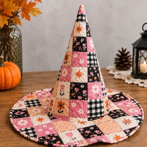 May include: A quilted witch hat featuring a patchwork design of pink, black, and peach squares. The fabric displays patterns of white flowers, black and white gingham checks, and orange star shapes. The hat has a tall conical crown and a wide brim.