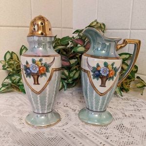 May include: A vintage salt and pepper shaker set with a green and white striped design. The shakers feature a gold trim and floral accents. The set is made of porcelain and has a iridescent finish.
