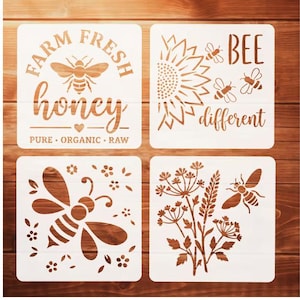May include: Four square white stencils featuring bee and floral designs. Top left reads FARM FRESH honey PURE ORGANIC RAW. Top right shows a sunflower and bees with text BEE different. Bottom left features a bee and flowers. Bottom right shows wildflowers and a bee.