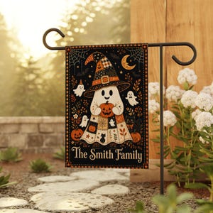 May include: A rectangular garden flag featuring a black background with a central ghost character wearing a patchwork witch hat and holding a pumpkin. The design includes small ghosts, cats, and autumn foliage. The text reads The Smith Family.