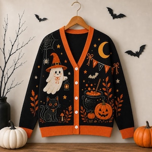 May include: A black V-neck cardigan with orange trim featuring a Halloween-themed pattern of a ghost wearing a hat, a black cat, a pumpkin, a cauldron, a crescent moon, stars, and a spider web. The garment has five white buttons down the front.