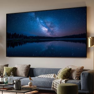 May include: A large rectangular wall art print featuring a night sky filled with stars and the Milky Way galaxy above a dark forest and a calm lake. The scene displays deep blue and purple hues with a clear reflection of the sky on the water.