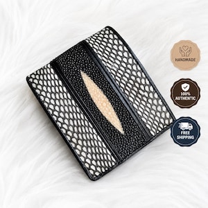 May include: A bi-fold wallet featuring a black and white snakeskin pattern on the outer panels, a central black textured strip, and a prominent, elongated, cream-colored stingray leather inlay running vertically down the center.