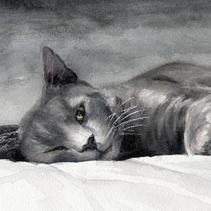 May include: Watercolor painting of a gray cat lying on a white surface. The cat is depicted in a relaxed pose, with its head tilted and eyes partially open. The artwork uses shades of gray and white, creating a soft, serene atmosphere.