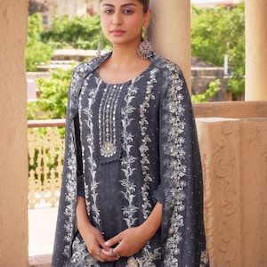 May include: A charcoal grey tunic featuring a white floral print, a central panel with vertical embroidery, and metallic embellishments. The garment includes a matching shawl draped over the shoulders, with intricate white botanical patterns.