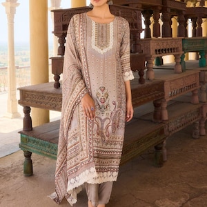 May include: A beige long-sleeved tunic featuring a brown and cream paisley print, a decorative neckline, and a matching shawl with a white lace border. The outfit includes solid light brown trousers and white open-toe sandals with a toe strap.