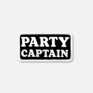 Peut inclure: Un écusson rectangulaire brodé avec un fond noir et une bordure blanche. Le texte PARTY CAPTAIN est cousu en lettres capitales blanches et grasses au centre de l'écusson. Le design présente une esthétique nette et contrastée.