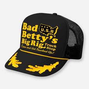 May include: A black trucker cap featuring a yellow graphic print that reads Bad Betty's Big Rig Truck Stop, Come and Get Trucked Up!, and a map of the U.S.A. The cap includes a yellow cord across the brim and yellow leaf-like embroidery.