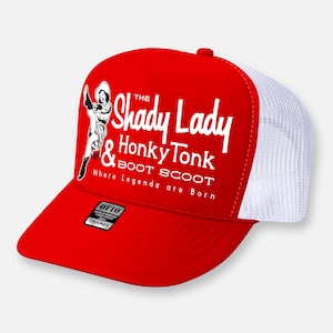 Op de afbeelding: Een rood-witte truckerpet met een witte afbeelding van een persoon met een hoed en laarzen, en de tekst The Shady Lady & Honky Tonk BOOT SCOOT Where Legends are Born. Een zwarte Otto-sticker bevindt zich op de klep van het rode voorpaneel.