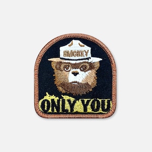 May include: An embroidered patch with a black background featuring the face of a brown bear wearing a white ranger hat with the text SMOKEY on the brim. Below the bear, the text ONLY YOU is embroidered in yellow with a black outline.