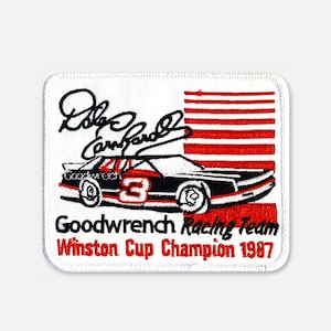 Könnte beinhalten: Ein rechteckiger gestickter Aufnäher mit einem schwarzen Rennwagen, der roten Nummer 3, einer Unterschrift und roten horizontalen Streifen. Der Text lautet: Goodwrench Racing Team Winston Cup Champion 1987. Mit weißem Hintergrund und Rand.