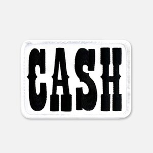 Pu&ograve; includere: Una toppa rettangolare ricamata con sfondo bianco e un bordo spesso cucito in bianco. La parola CASH &egrave; visualizzata in grandi lettere maiuscole nere in grassetto con un distinto stile di carattere serif centrato sulla superficie della toppa.