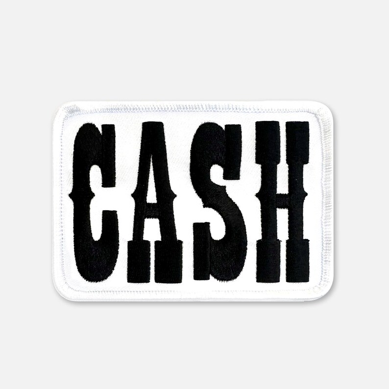 Pu&ograve; includere: Una toppa rettangolare ricamata con sfondo bianco e un bordo spesso cucito in bianco. La parola CASH &egrave; visualizzata in grandi lettere maiuscole nere in grassetto con un distinto stile di carattere serif centrato sulla superficie della toppa.