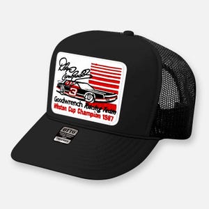 May include: A black trucker hat featuring a rectangular patch with a graphic of a race car numbered 3, a signature, and red horizontal stripes. The text reads Goodwrench Racing Team Winston Cup Champion 1987. An Otto brand sticker is on the brim.