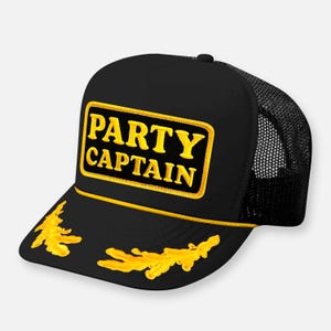 May include: A black trucker hat featuring a rectangular patch with the yellow embroidered text PARTY CAPTAIN. The hat includes a yellow braided cord across the base of the front panel and yellow embroidered leaf designs on the brim.