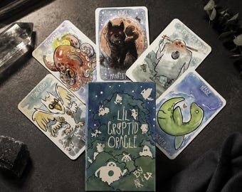 May include: A deck of Lil Cryptid Oracle cards featuring a box with green forest illustrations and five individual cards displaying watercolor-style drawings of creatures including an octopus, a wolf, a mothman, and a sea serpent with text.