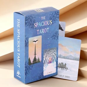 以下が含まれることがあります： 「The Spacious Tarot」と題された青いタロットカードデッキの箱。装飾的な花の模様が施されています。箱には2枚のカードのイラストが描かれており、1枚は剣と鳥、もう1枚は雪道です。箱の横には「Four of Swords」のカードが立てかけられています。