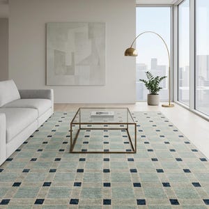 K&ouml;nnte beinhalten: Ein rechteckiger Teppich mit einem Gittermuster aus hellblauen und beigen Quadraten, wobei sich an jeder Kreuzung kleine, dunkelmarineblaue Quadrate befinden. Der Teppich hat an der Unterkante kurze, helle Fransen und eine gewebte Oberfl&auml;che.