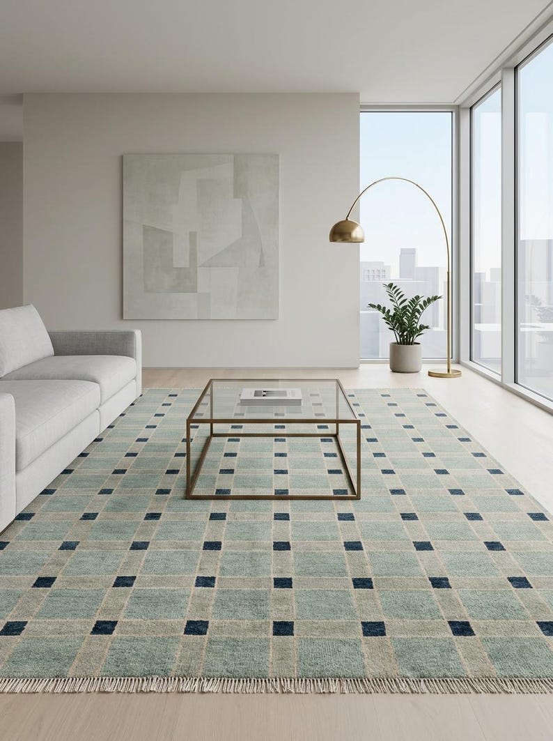 K&ouml;nnte beinhalten: Ein rechteckiger Teppich mit einem Gittermuster aus hellblauen und beigen Quadraten, wobei sich an jeder Kreuzung kleine, dunkelmarineblaue Quadrate befinden. Der Teppich hat an der Unterkante kurze, helle Fransen und eine gewebte Oberfl&auml;che.