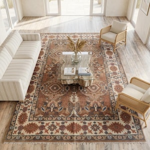 Könnte beinhalten: Ein großer rechteckiger Teppich mit einem komplexen, traditionellen Muster in Rost-, Creme- und Dunkelblautönen. Der Teppich hat eine breite dekorative Bordüre mit geometrischen Motiven und einem zentralen Medaillon-Design sowie kurze Fransen.