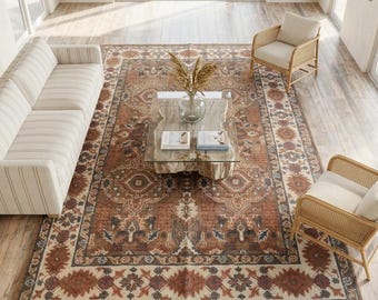 May include: A large rectangular area rug featuring a complex, traditional-style pattern in shades of rust, cream, and dark blue. The rug has a wide decorative border with geometric motifs and a central medallion design, finished with short fringe edges.