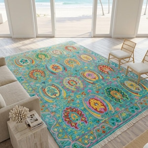 Könnte beinhalten: Ein rechteckiger Teppich mit einem leuchtend türkisfarbenen Hintergrund und einem sich wiederholenden Muster aus bunten, stilisierten Blumen- und Paisley-Motiven in Rot, Gelb, Orange und Grün, mit weißen Fransen an den kurzen Seiten.