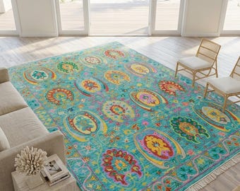 May include: A rectangular area rug featuring a vibrant turquoise background with a repeating pattern of colorful, stylized floral and paisley motifs in shades of red, yellow, orange, and green, finished with white fringe along the short edges.
