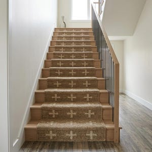 May include: A staircase with light wood treads and a central jute runner featuring a repeating white cross pattern. The stairs include a wooden handrail with vertical black metal balusters, leading upward towards a bright window at the landing.