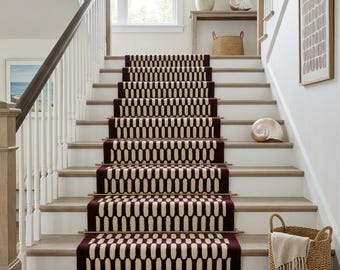 May include: A staircase featuring a runner with a repeating dark maroon and cream oval pattern. The runner is secured to the wooden steps with metallic gold rods. The staircase has white railings with a dark wood handrail and white risers.