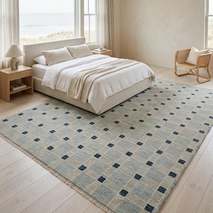 K&ouml;nnte beinhalten: Ein rechteckiger Teppich mit einem Gittermuster aus hellblauen und beigen Quadraten, das an jeder Kreuzung mit kleinen, dunkel marineblauen Quadraten akzentuiert ist. Der Teppich hat kurze Fransen an den Kanten und eine strukturierte Weboptik.