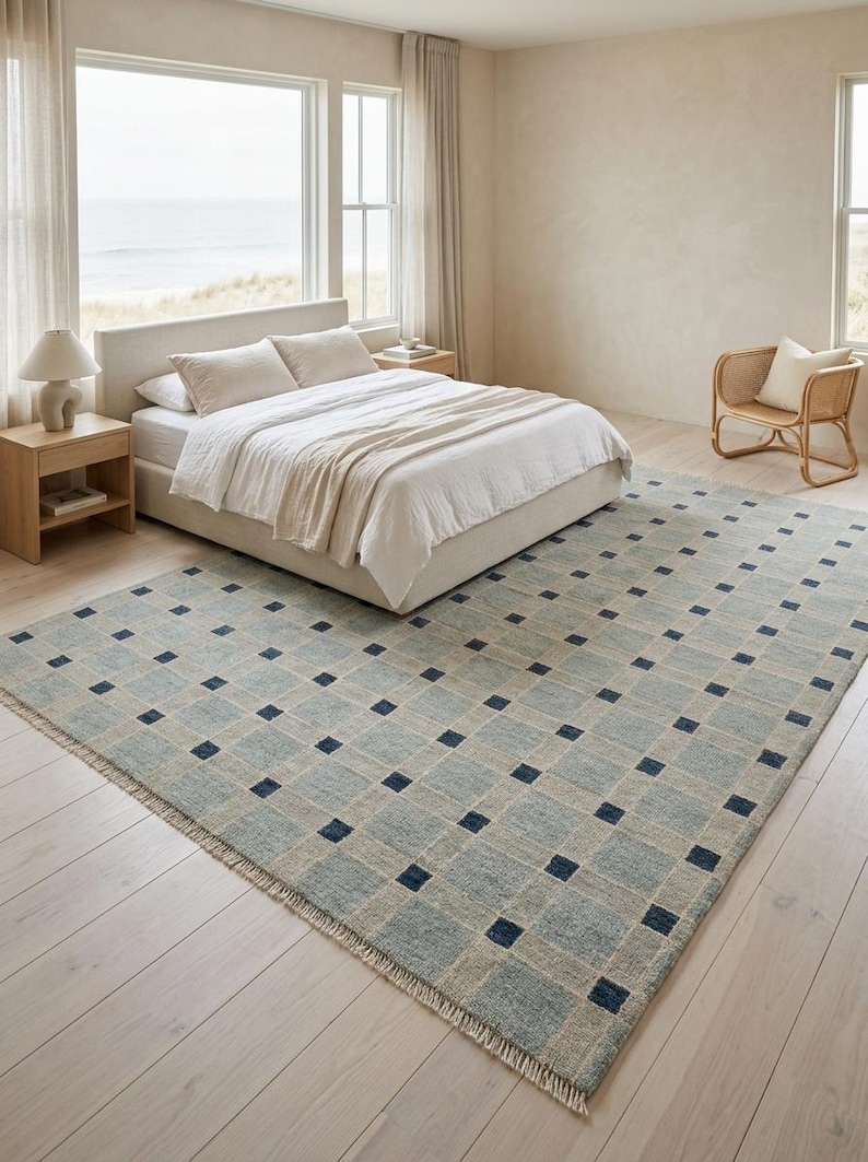 K&ouml;nnte beinhalten: Ein rechteckiger Teppich mit einem Gittermuster aus hellblauen und beigen Quadraten, das an jeder Kreuzung mit kleinen, dunkel marineblauen Quadraten akzentuiert ist. Der Teppich hat kurze Fransen an den Kanten und eine strukturierte Weboptik.