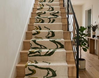 May include: A staircase with light wood steps and a central runner featuring a cream-colored base with abstract, flowing patterns in dark green and olive green. A black metal railing runs along the right side of the stairs.