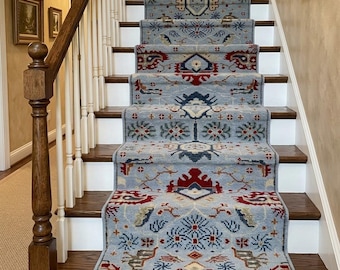 Puede incluir: Una alfombra larga para escaleras con fondo azul claro y patrones intrincados en rojo, azul oscuro y crema. La alfombra cubre el centro de los escalones de madera con contrahuellas blancas y tiene un borde con flecos en la parte inferior.