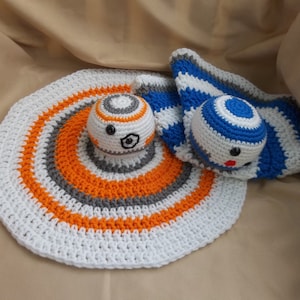 Puede incluir: Una manta de bebé de crochet blanca, naranja y gris con un personaje BB-8 de crochet blanco, naranja y gris y un personaje BB-8 de crochet azul y blanco.