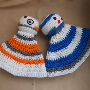 Puede incluir: Dos juguetes de peluche tejidos a crochet, uno con rayas naranjas, blancas y grises y el otro con rayas azules, blancas y grises. Ambos juguetes tienen una cabeza redonda con una cara.