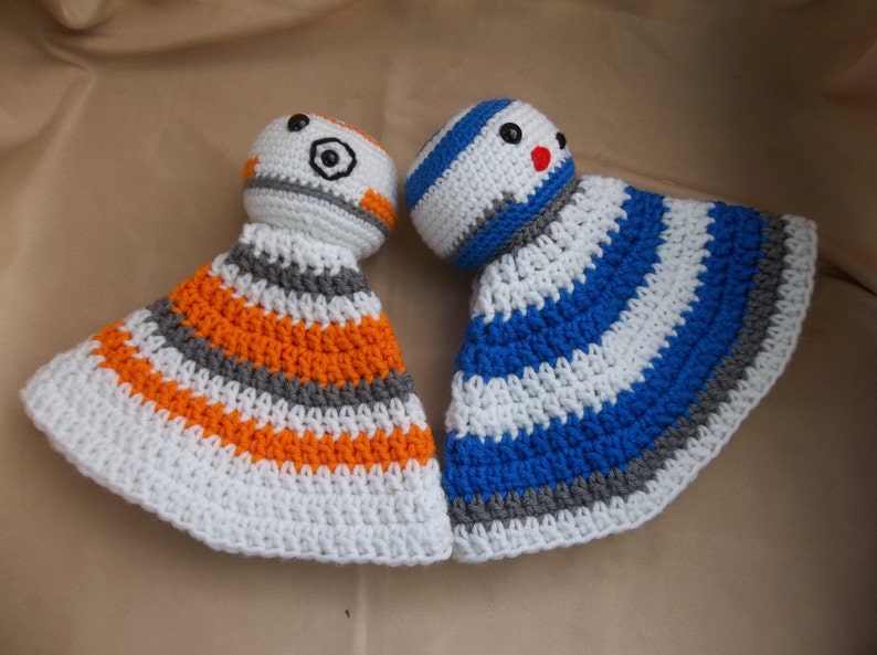 Puede incluir: Dos juguetes de peluche tejidos a crochet, uno con rayas naranjas, blancas y grises y el otro con rayas azules, blancas y grises. Ambos juguetes tienen una cabeza redonda con una cara.