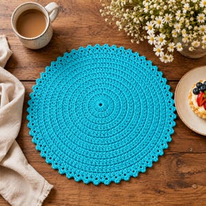 May include: A circular, bright turquoise crochet doily featuring a textured, concentric stitch pattern and a scalloped edge. The piece is crafted with a consistent yarn weight and displays a uniform, vibrant blue-green color throughout its design.
