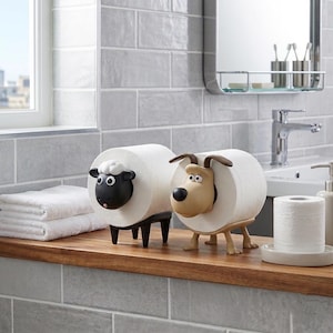 May include: Two toilet paper holders shaped like animals. One is a black sheep with white woolly hair, and the other is a tan dog with brown ears. Each holder features a central cylindrical body designed to hold a roll of white toilet paper.