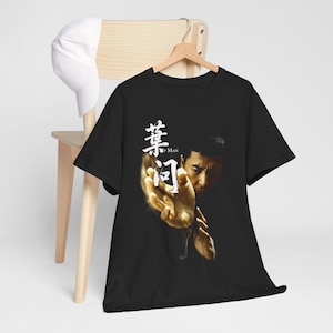 May include: A black short-sleeved t-shirt featuring a graphic print of a martial artist in a defensive stance. The design includes white Chinese characters and the text "IP MAN" positioned next to the figure's outstretched hand.
