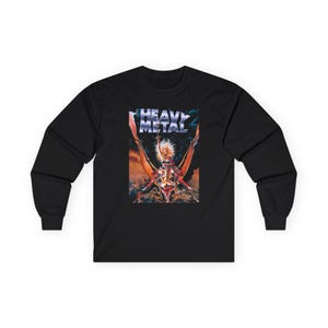 May include: A black long-sleeve shirt featuring a graphic print of a person with blonde hair holding a sword while riding a winged creature. Above the figure, the text HEAVY METAL is printed in a metallic, stylized font against a dark background.