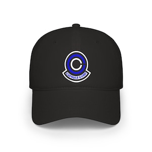 Puede incluir: Una gorra de béisbol negra con un logotipo centrado que presenta un diseño circular blanco y azul y el texto CAPSULE CORP. en letras azules. La gorra tiene una corona estructurada, una visera curva y un botón en la parte superior central.