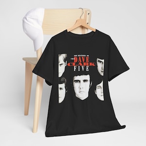 Op de afbeelding: Een zwart T-shirt met korte mouwen en een zwart-witte grafische print van de bandleden van The Dave Clark Five, met de tekst The History of The Dave Clark Five in rode en witte letters. Een effen witte baseballpet hangt erbij.