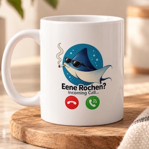 Könnte beinhalten: Ein weißer Keramikbecher mit einer Grafik eines blauen Rochen, der eine schwarze Sonnenbrille trägt und eine Zigarette raucht. Unter dem Rochen steht der Text Eene Rochen? Incoming Call... mit einem roten und grünen Telefon-Symbol.
