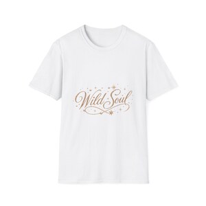 Op de afbeelding: Een wit T-shirt met korte mouwen en de tekst Wild Soul in een metallic koperkleurig cursief lettertype. Het ontwerp is versierd met kleine stervormen en stippen, wat een decoratieve afbeelding vormt in het midden van het kledingstuk.