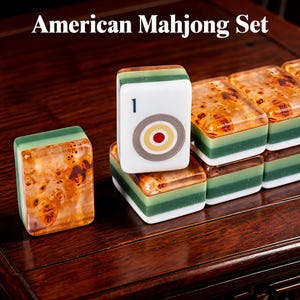 May include: An American Mahjong Set featuring rectangular tiles with a white face displaying a number one and a circular target graphic. The tiles have a layered design with a green middle section and a translucent amber-colored burl wood pattern.