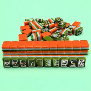 May include: A collection of rectangular mahjong tiles featuring a tri-color design of orange, white, and olive green. Some tiles are arranged in neat rows, while others are scattered in a pile. The front-facing tiles display various symbols.